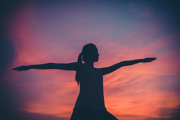 La siluetta della donna asiatica gioca a yoga sul tramonto