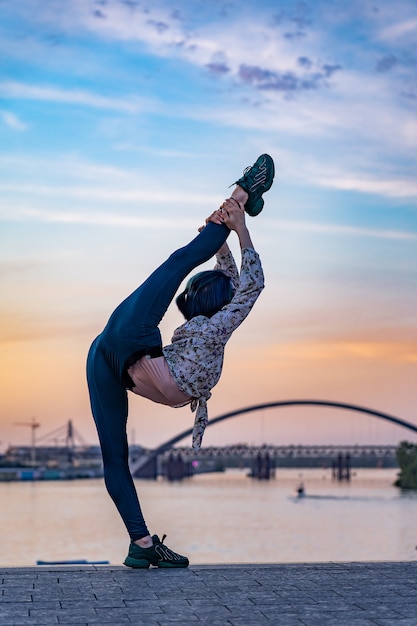 La siluetta della donna femminile flessibile mantiene l'equilibrio ginnico sulla spaccatura sul drammatico concetto di tramonto ...