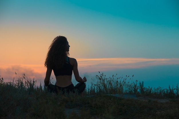 La siluetta della giovane donna sta praticando lo yoga al tramonto