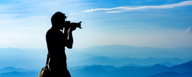 La siluetta di un fotografo con zaino e sacco a pelo con le montagne mette il fondo sullo strato durante il tramonto