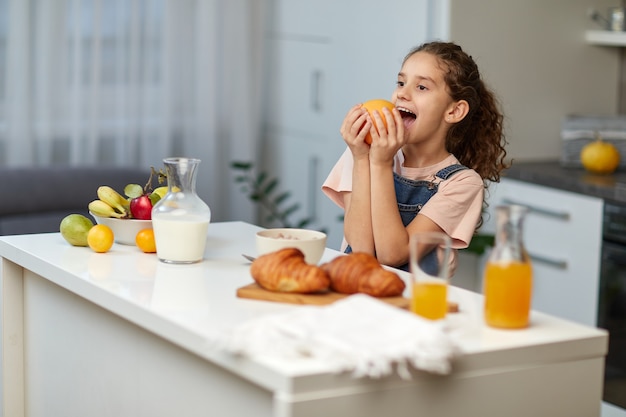 La simpatica bambina con i capelli ricci, fa colazione insieme alla mamma in cucina, prova a mangiare un frutto.