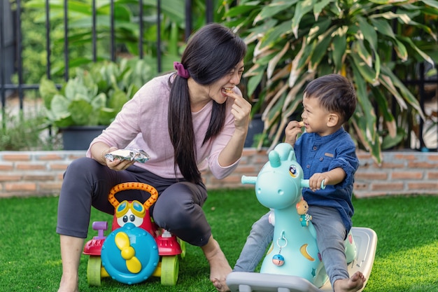 La singola mamma asiatica con il figlio sta giocando con il giocattolo e sta mangiando insieme vivendo nel prato anteriore