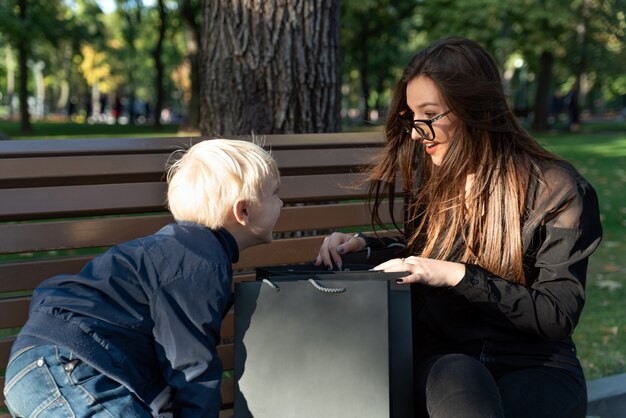 La sorella maggiore e suo fratello sono seduti su una panchina nel parco e guardano la borsa della spesa