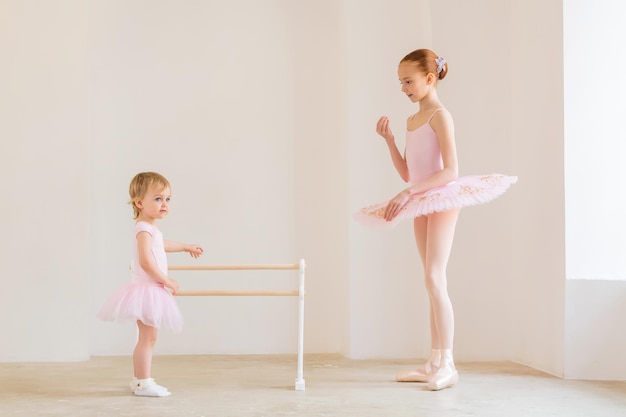 La sorella maggiore, una ballerina in tutù rosa e scarpe da punta, mostra al bambino come esercitarsi alla sbarra