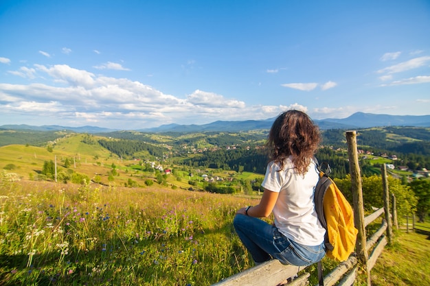 La splendida ragazza felice gode della vista delle colline seduta in un campo di fiori sulla collina con un paesaggio naturale mozzafiato.