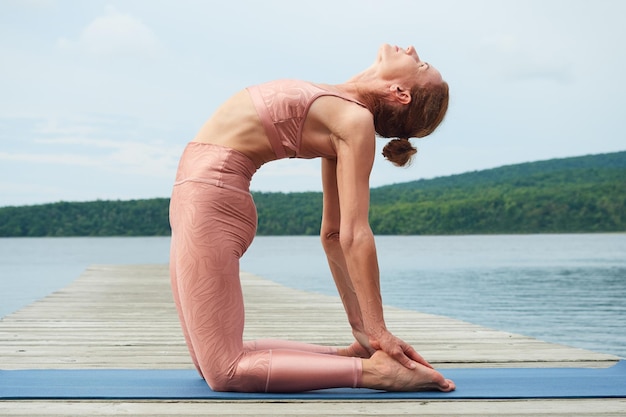 La sportiva in abbigliamento sportivo rosa pratica lo yoga vicino al mare all'aperto