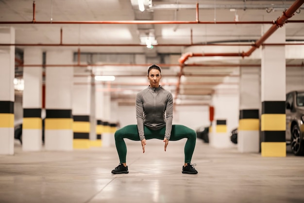 La sportiva muscolare in abbigliamento sportivo sta facendo allenamenti per le gambe nel garage sotterraneo