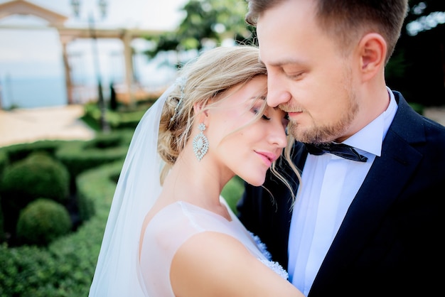 La sposa bionda tenera si appoggia alla spalla dello sposo che sta nel giardino verde dell&#39;estate