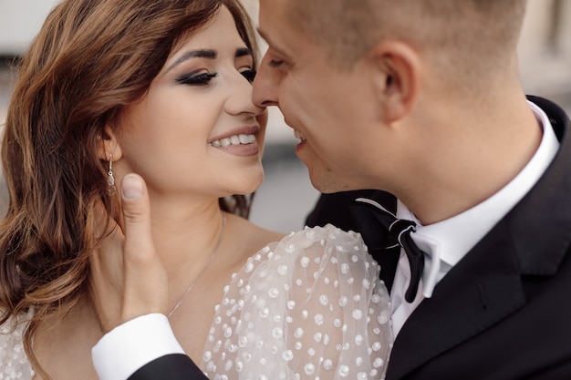 La sposa carina con un sorriso in abito da sposa riceve un bacio da uno sposo in giacca e cravatta. Foto tenerezza, amore felicità. Il giorno del matrimonio concetto.