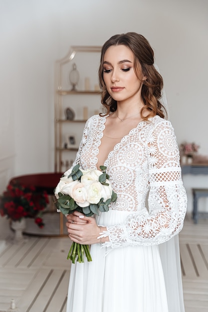 La sposa con un bouquet di fiori freschi in un bellissimo abito festivo con pizzo.