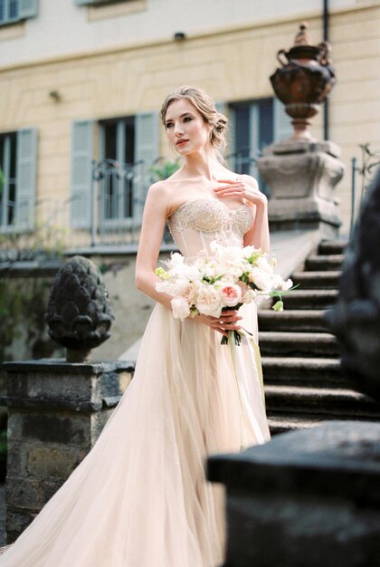 La sposa con un bouquet si trova sui gradini di fronte a un'antica villa Como Italia