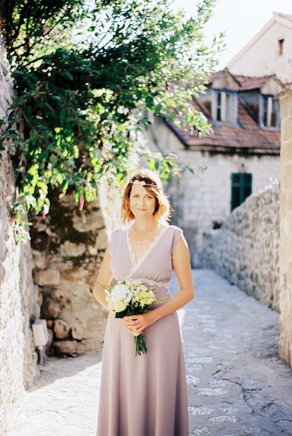 La sposa con un mazzo di fiori si trova sulla stradina di una città vecchia