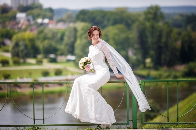 La sposa della giovane bella ragazza in vestito bianco resta sulla costa dell'ampio fiume e aspetta lo sposo La sposa su un'alta scogliera vicino al fiume Il giorno più bello della giovane donna