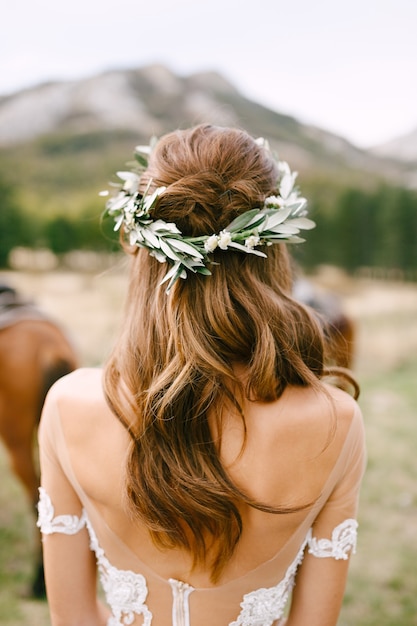 La sposa è in piedi con la schiena in un bellissimo abito di pizzo, la testa della sposa è adornata con una corona di fiori