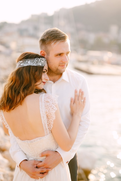 La sposa e lo sposo che si abbracciano delicatamente sullo sfondo del molo delle barche a Budva, la sposa ha messo