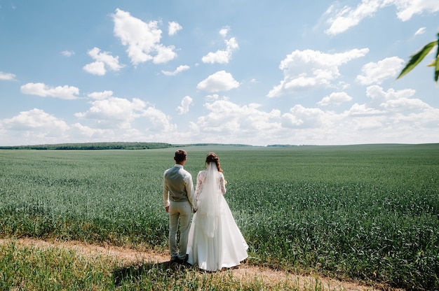 La sposa e lo sposo con un bouquet da sposa, tenendosi per mano e in piedi indietro a guardare le montagne.