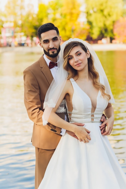 La sposa e lo sposo felici alla moda che posano al grande amore esprimono alla sera si accendono al ricevimento nuziale all'aperto. Splendide sposi di sposi divertendosi nel parco di sera.