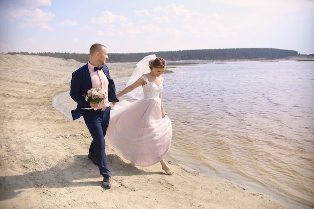 La sposa e lo sposo felici corrono lungo il lago shore