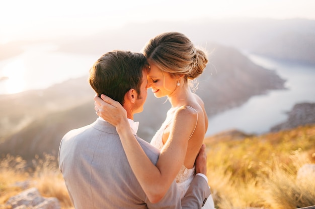 La sposa e lo sposo seduti sulla cima del monte lovcen con vista sulla baia di kotor sorridendo e