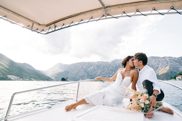 La sposa e lo sposo si baciano mentre sono seduti sulla prua di uno yacht che naviga sul mare