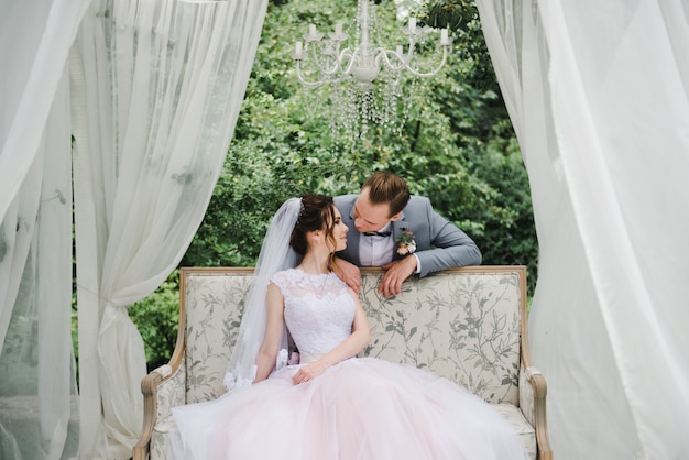 La sposa e lo sposo sono seduti su un bellissimo divano in un gazebo in giardino