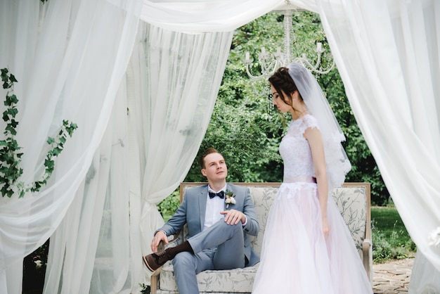 La sposa e lo sposo sono seduti su un bellissimo divano in un gazebo in giardino