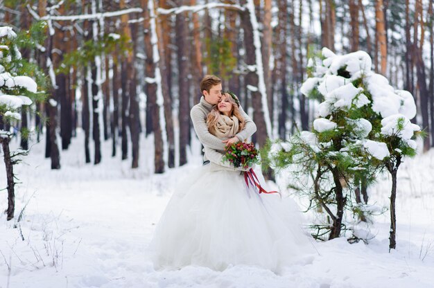 La sposa e lo sposo stanno sedendo sul tronco nella foresta dell'inverno.