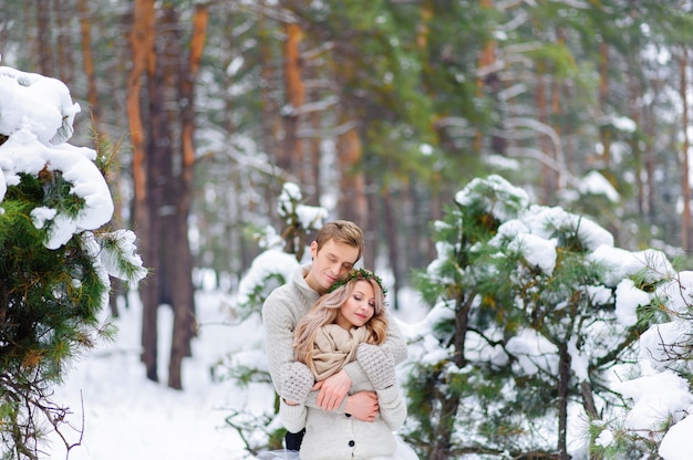 La sposa e lo sposo stanno sedendo sul tronco nella foresta dell'inverno.