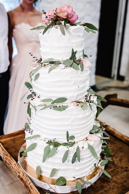 La sposa e lo sposo stanno tagliando la loro torta nuziale rustica sul banchetto nuziale Le mani tagliano la torta bianca con delicati fiori rosa