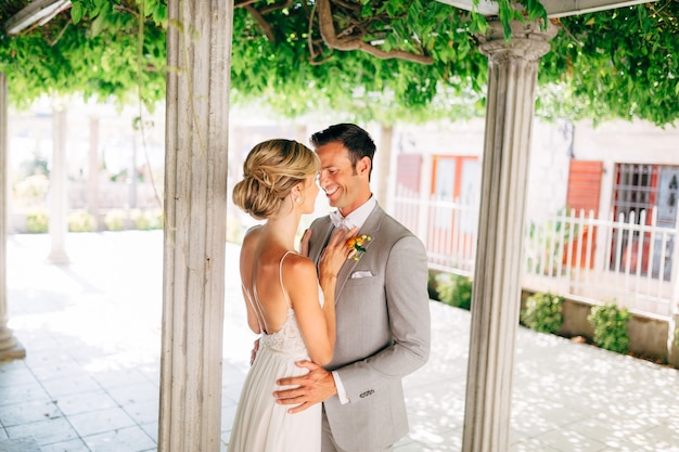 La sposa e lo sposo stanno tra le colonne abbracciando e sorridendo la sposa