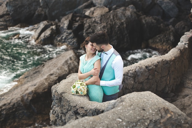 La sposa e lo sposo sulla natura in montagna vicino all'acqua. Abito e vestito colore Tiffany. Baci e abbracci.