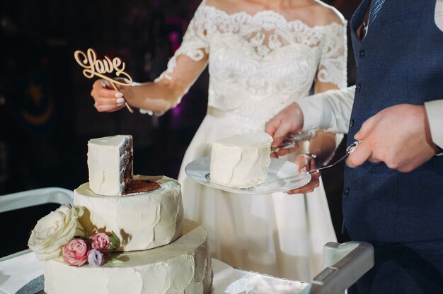 La sposa e lo sposo tagliano la loro torta nuziale. bella torta con un taglio e ripieno a vista. torta nuziale con la parola amore, il concetto del matrimonio.