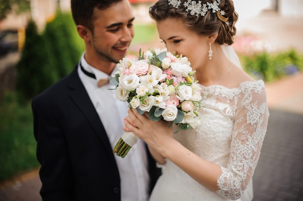 La sposa gode del profumo di un bouquet da sposa, lo sposo si trova accanto a sorridere