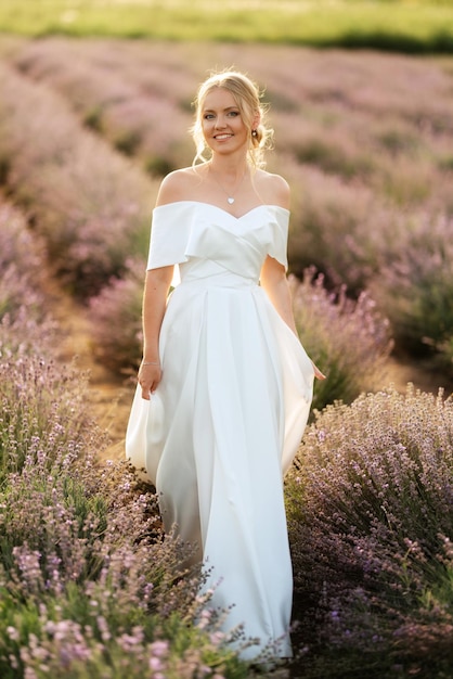 La sposa in abito bianco cammina sul campo di lavanda