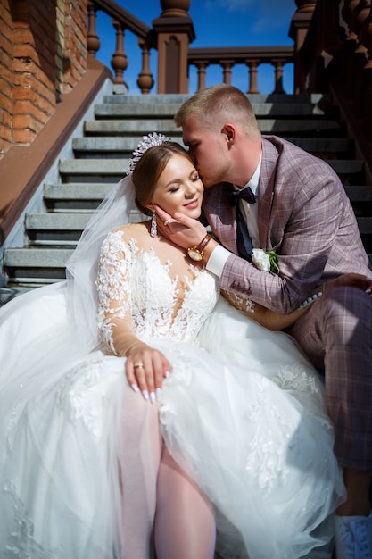 La sposa in abito bianco e lo sposo in costume si abbracciano sui gradini