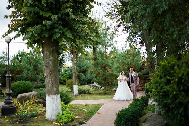 La sposa in abito bianco e lo sposo in costume si coccolano e passeggiano nel parco