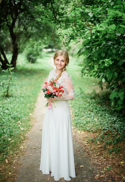 La sposa in abito bianco lungo posa con bouquet rosso sul pass