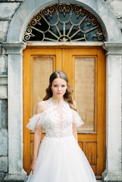 La sposa in abito bianco si trova davanti a una porta di legno di un edificio in pietra
