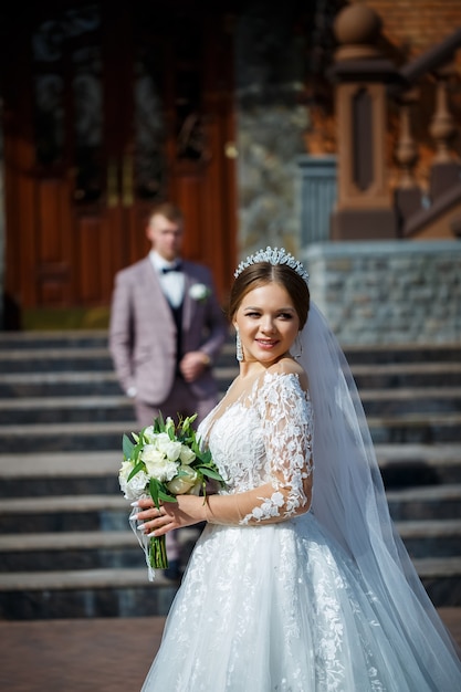 La sposa in abito da sposa bianco e lo sposo in abito sullo sfondo di un edificio in mattoni con ampi gradini