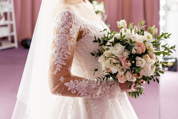 La sposa in abito da sposa bianco tiene tra le mani il suo bouquet da sposa