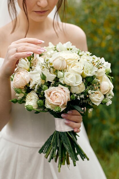 La sposa in abito da sposa con le spalle aperte tiene un mazzo di rose