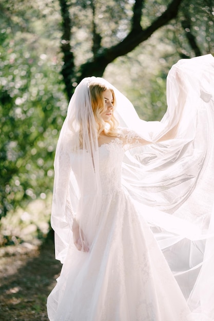 La sposa in abito di pizzo bianco tiene il velo con la mano