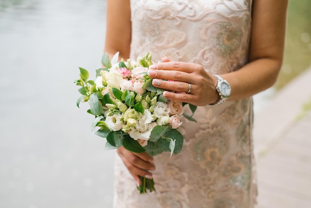 La sposa in un abito da sposa beige tiene in mano un mazzo di fiori e verde