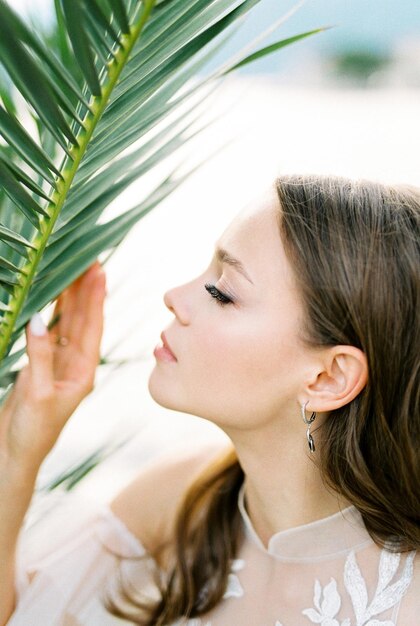 La sposa in un abito di pizzo bianco tocca un ramo di palma verde