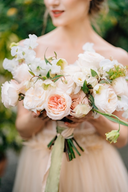 La sposa in un bel vestito tiene in mano un mazzo di fiori rosa