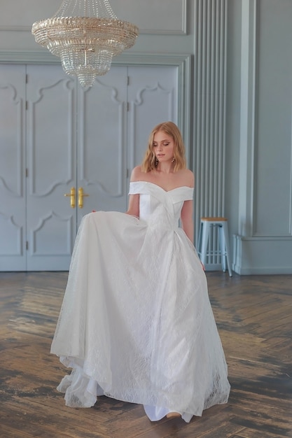 La sposa in un bellissimo abito da sposa bianco entra nella sala tenendo l'orlo del vestito