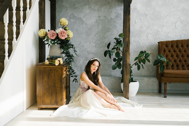 La sposa in un bellissimo abito da sposa bianco si siede a piedi nudi sul pavimento