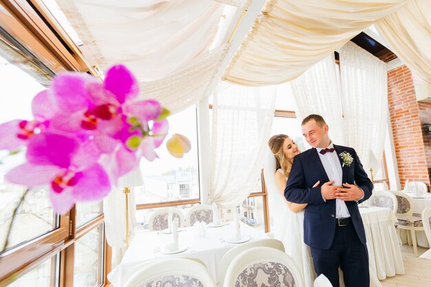 La sposa in un bellissimo vestito abbraccia lo sposo dal retro della sala del ristorante