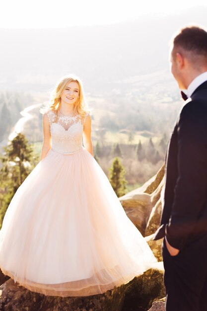 La sposa in un vestito con pizzo guarda lo sposo su uno sfondo di montagne