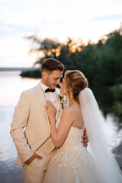 La sposa in un vestito gonfio bianco e lo sposo in t sulla riva del fiume